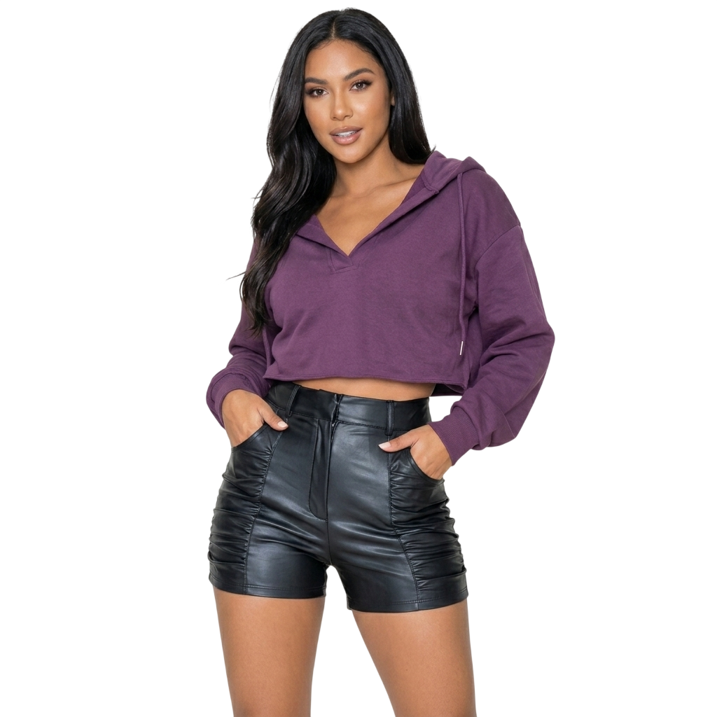A woman posing in high waisted black genuine leather shorts with side ruched detailing and a purple cropped hoodie, shown on a pure white background