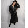 Stylish woman wearing a long black faux leather trench coat with a belted waist, standing against a white backdrop.